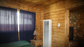 Una camera di una baita in legno con un letto, un comodino con una lampada, un riscaldatore a parete e un muro in pietra.