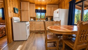 Interior de una cabaña de madera con cocina, comedor y una cama.