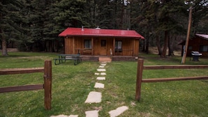 Una cabaña de madera con techo rojo, una mesa de picnic y un camino de piedra que lleva a la entrada.