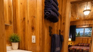 Interior de madera con un lavamanos, una planta en maceta, toallas y una cama con vistas.