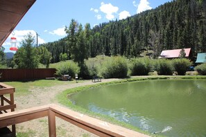 Eine Holzterrasse mit einer Bank, einem Teich, einem Gebäude mit rotem Dach und einem bewaldeten Hang.