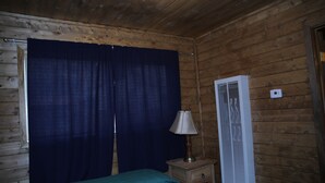 A room with a bed, a nightstand, a lamp, a window with curtains, and a wall-mounted air conditioner. - Located on our Private Fishing Pond (Red River)