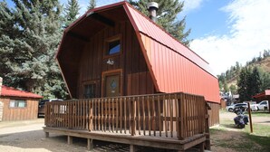 Une cabane en bois avec un toit rouge, une porte d’entrée et un balcon doté d’une balustrade en bois.