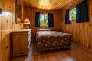 Une chambre dans une cabane en bois, avec un lit, une commode et des fenêtres avec des rideaux.