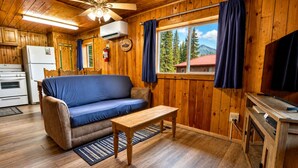 Ein Ferienhausinnenraum mit Sofa, Holztisch, Deckenventilator und einem Fenster mit Vorhängen.