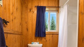 Ein Badezimmer aus Holz mit Toilette, einem Fenster, einer Duschvorhang und einem Handtuchhalter.