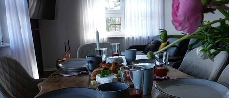 Ein Esstisch ist gedeckt mit Tellern, Tassen und Gläsern, mit einem Blumenstrauß und einer Kerze darauf.