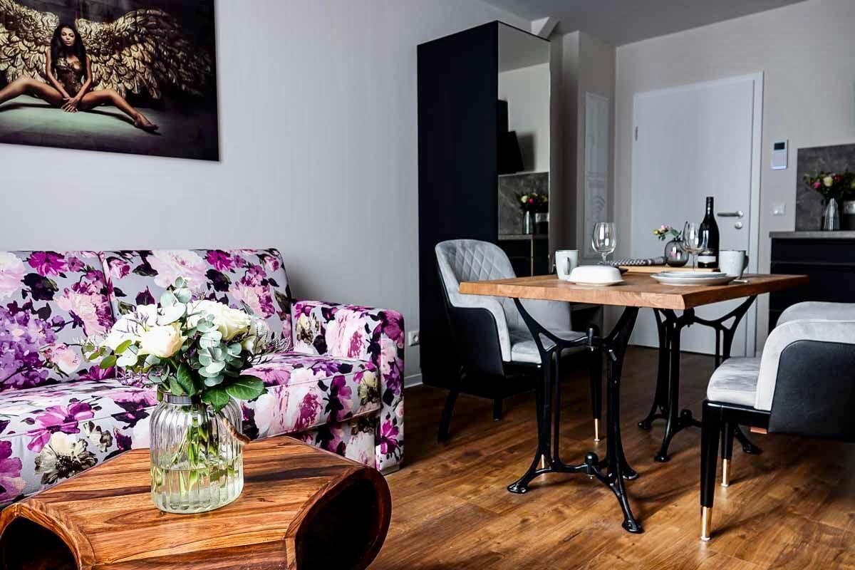 Una sala de estar moderna con un sofá floral, una mesa de centro de madera y un comedor con una mesa y sillas de madera.