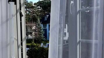 Ein Fenster mit transparenten Vorhängen, das einen Blick auf eine Wohngegend mit Häusern und Bäumen freigibt.