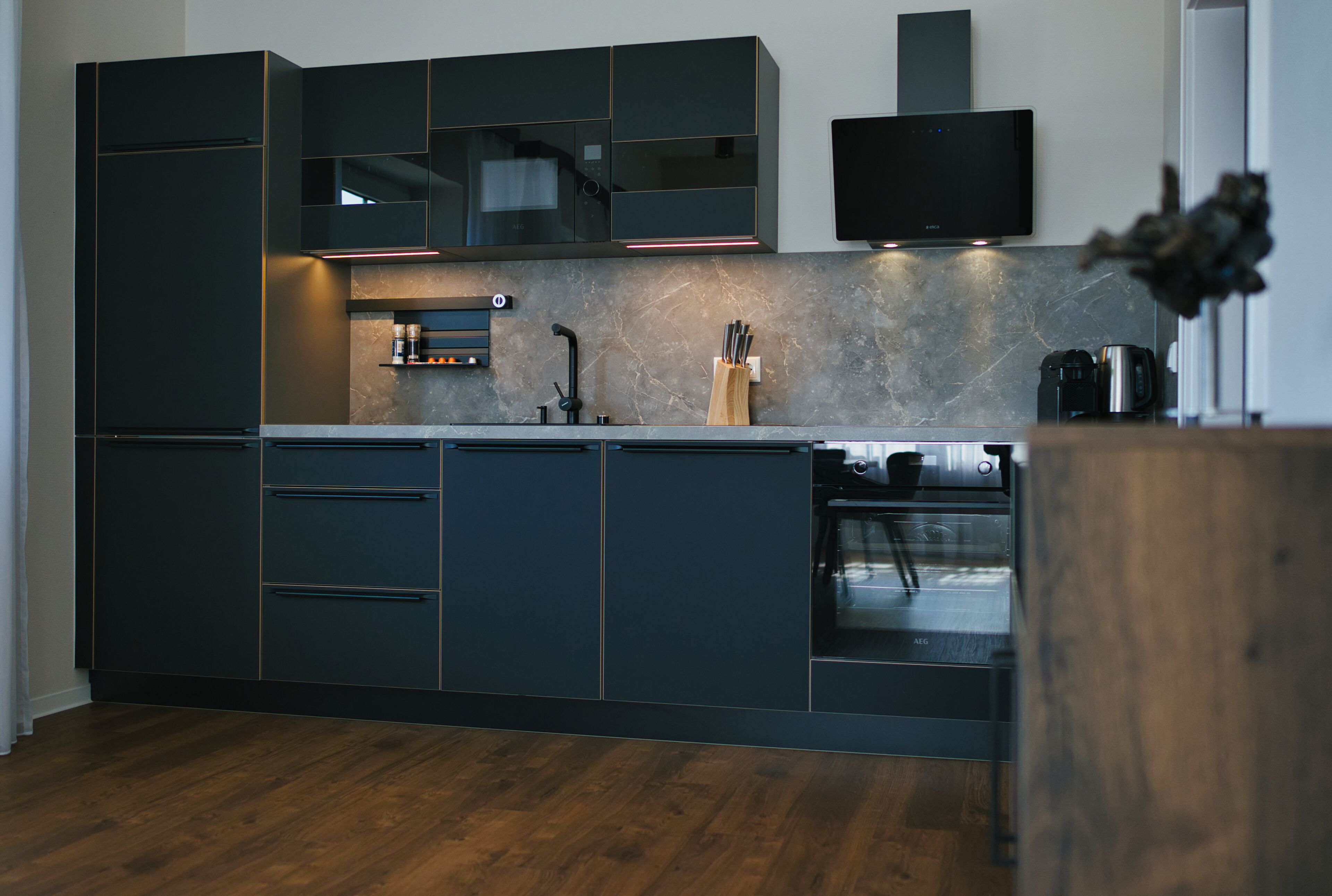 Una cocina moderna con armarios oscuros, horno empotrado y un televisor de pantalla plana sobre la encimera.