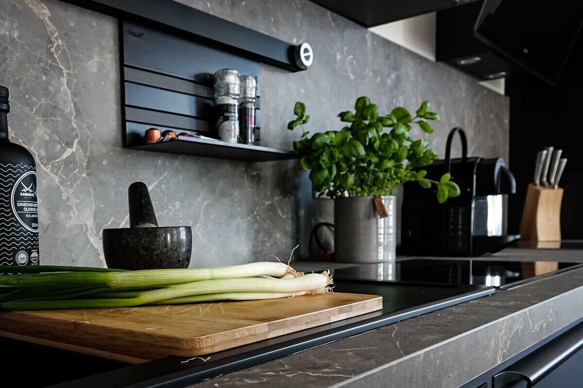 Una encimera de cocina con una tabla de cortar de madera, un mortero y una manoja, una planta en maceta y una botella de aceite de oliva.