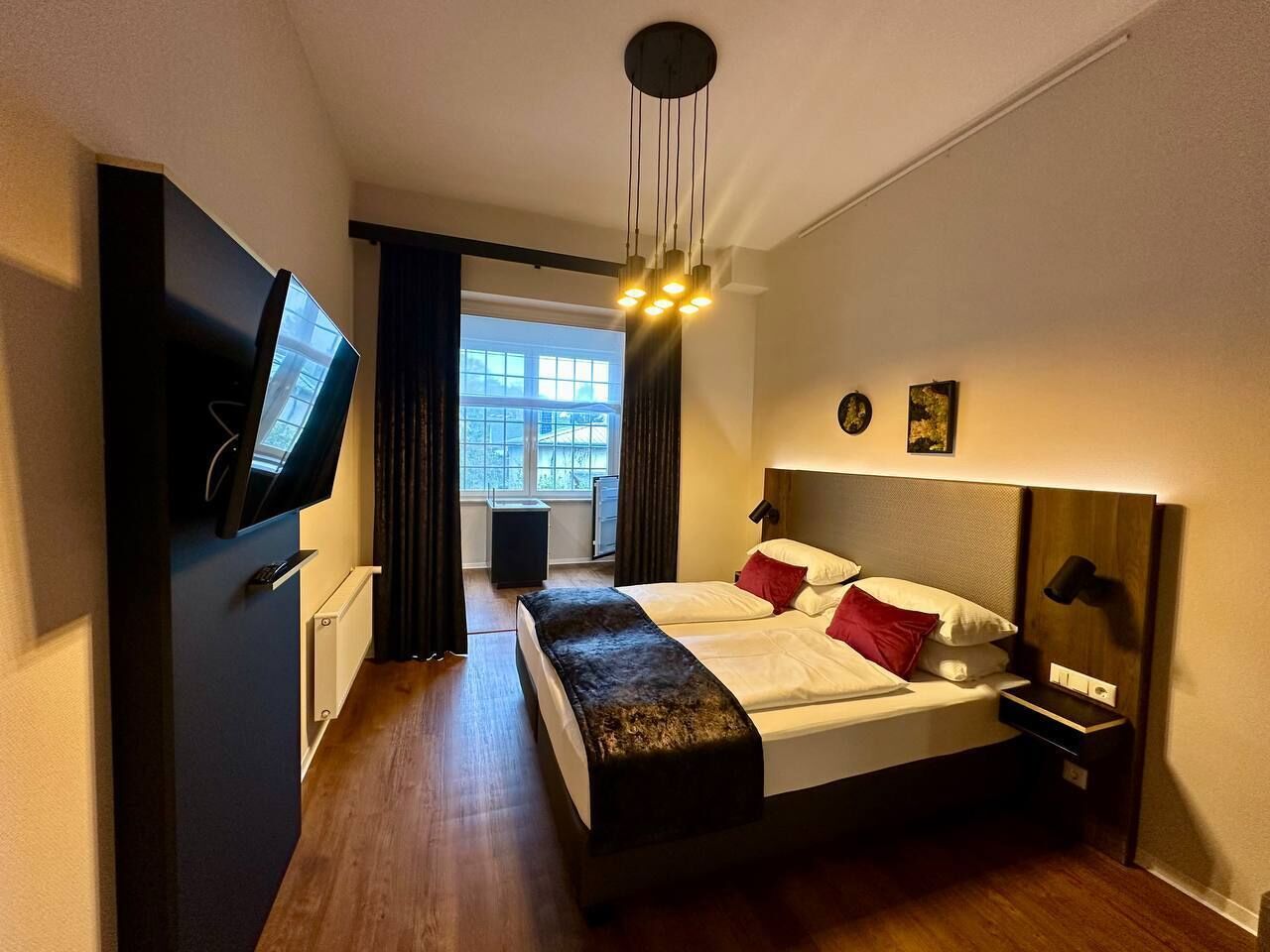 A modern hotel room with a large bed, a flat-screen TV, a bedside table, and a window with curtains.