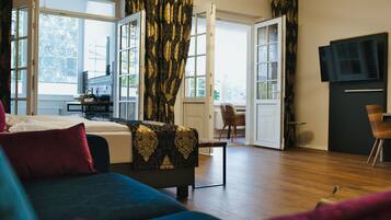 Ein modernes Wohnzimmer mit Sofa, Couchtisch und Fernseher. Ein großes Fenster mit Vorhängen, eine Tür zu einem anderen Raum und ein kleiner Tisch mit Lampe sind ebenfalls vorhanden.