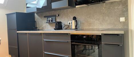 Una cocina moderna con armarios oscuros, horno empotrado y cafetera.
