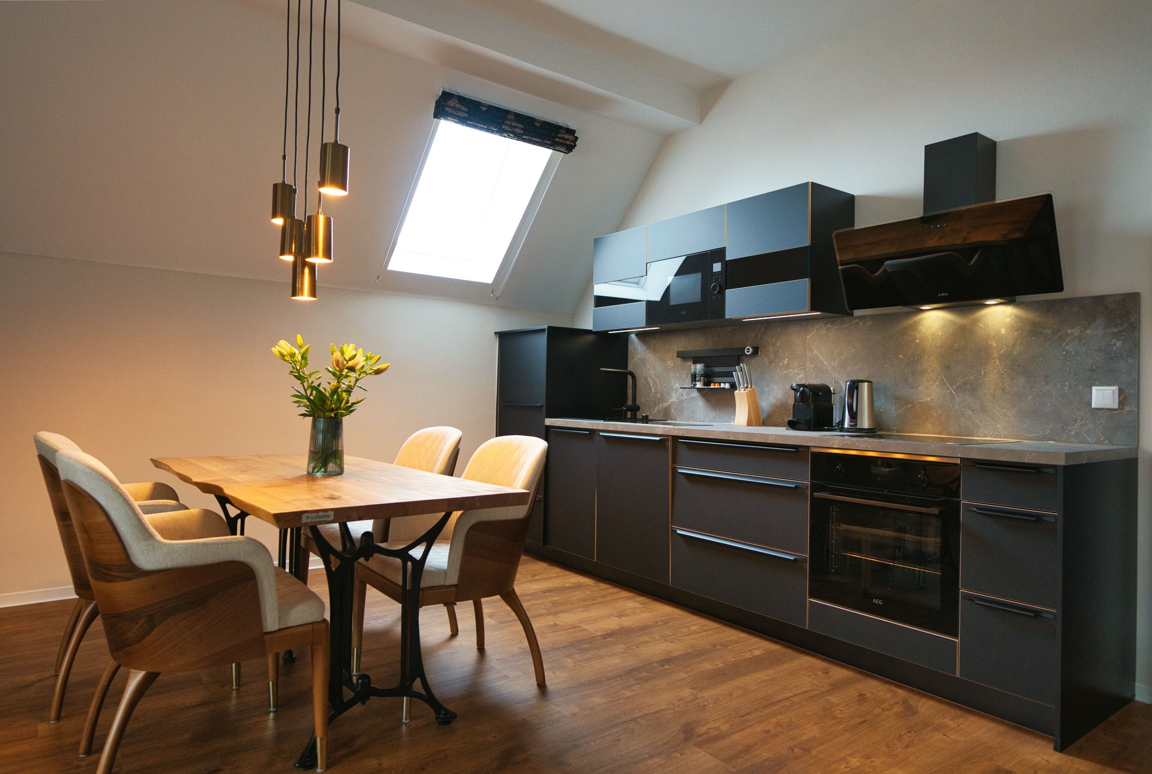 A modern kitchen with a dining area, featuring a skylight, dark cabinetry, and a wooden dining table with chairs.