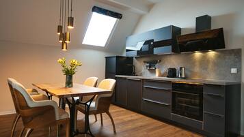 A modern kitchen with a dining area, featuring a skylight, dark cabinetry, and a wooden dining table with chairs.