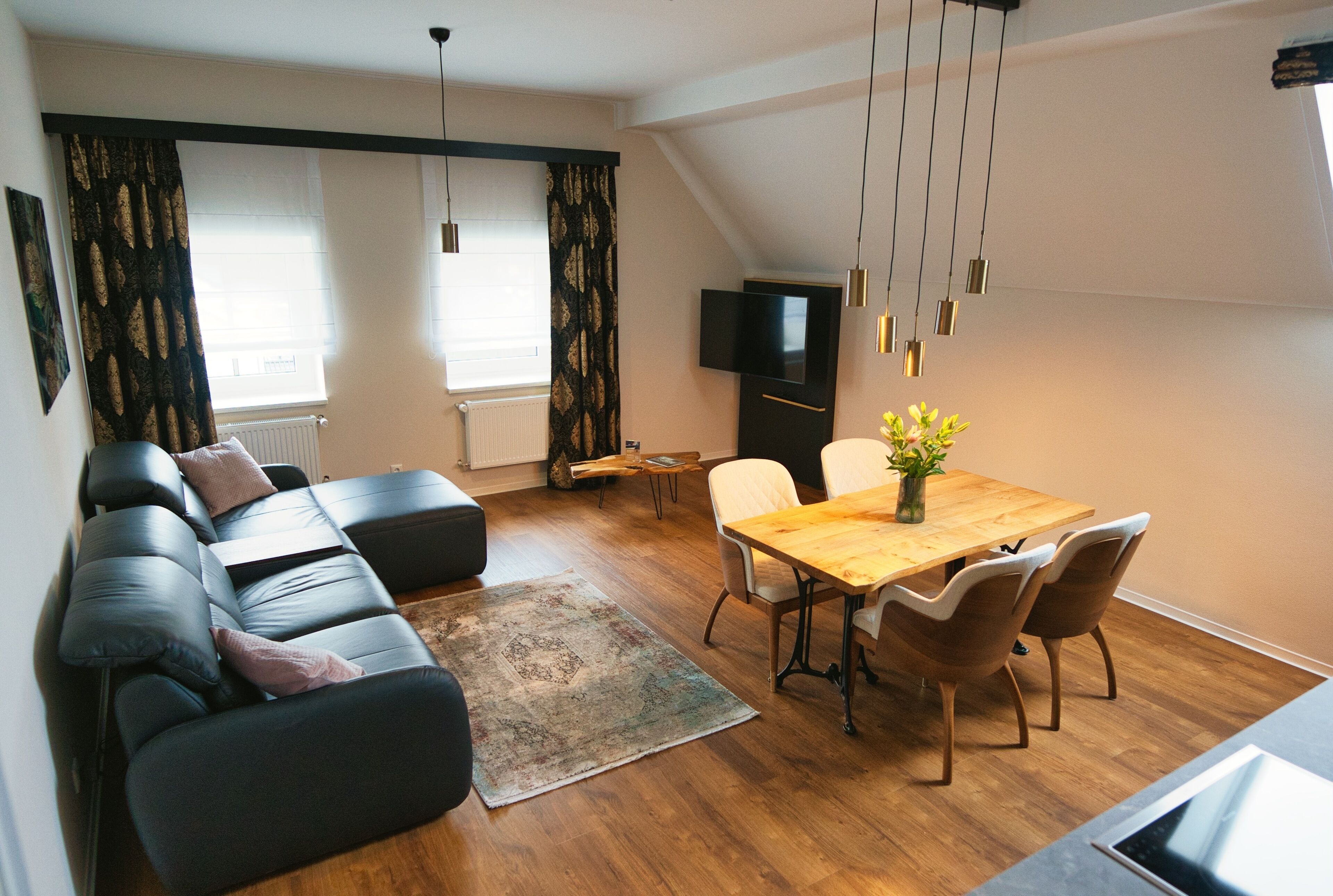 A modern living room with a sofa, dining table, and chairs. There is a television on the wall and a plant on the table.