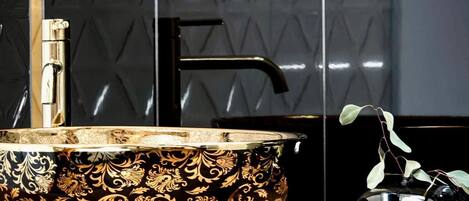 A black and gold ornate bowl on a wooden surface, a black faucet, and a glass vase with a plant.