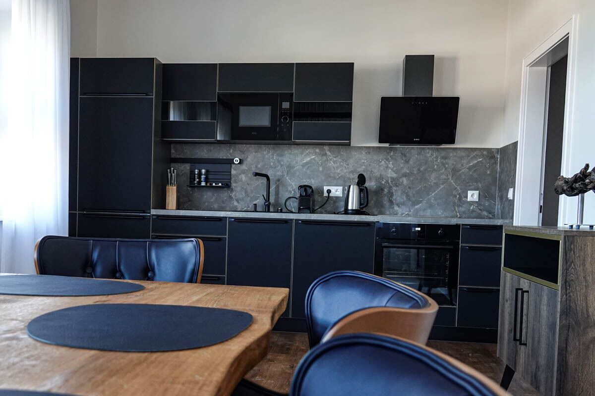 A modern kitchen with dark cabinetry, a wooden dining table, and blue chairs.