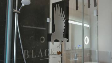 Een badkamer met een glazen scheidingswand waarop een witte silhouet van een vogel met kroon is afgebeeld, en de tekst 'BLACK EAGLE' is zichtbaar.