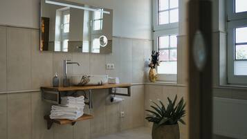 A modern bathroom with a large mirror, a sink, a towel rack, and a potted plant.
