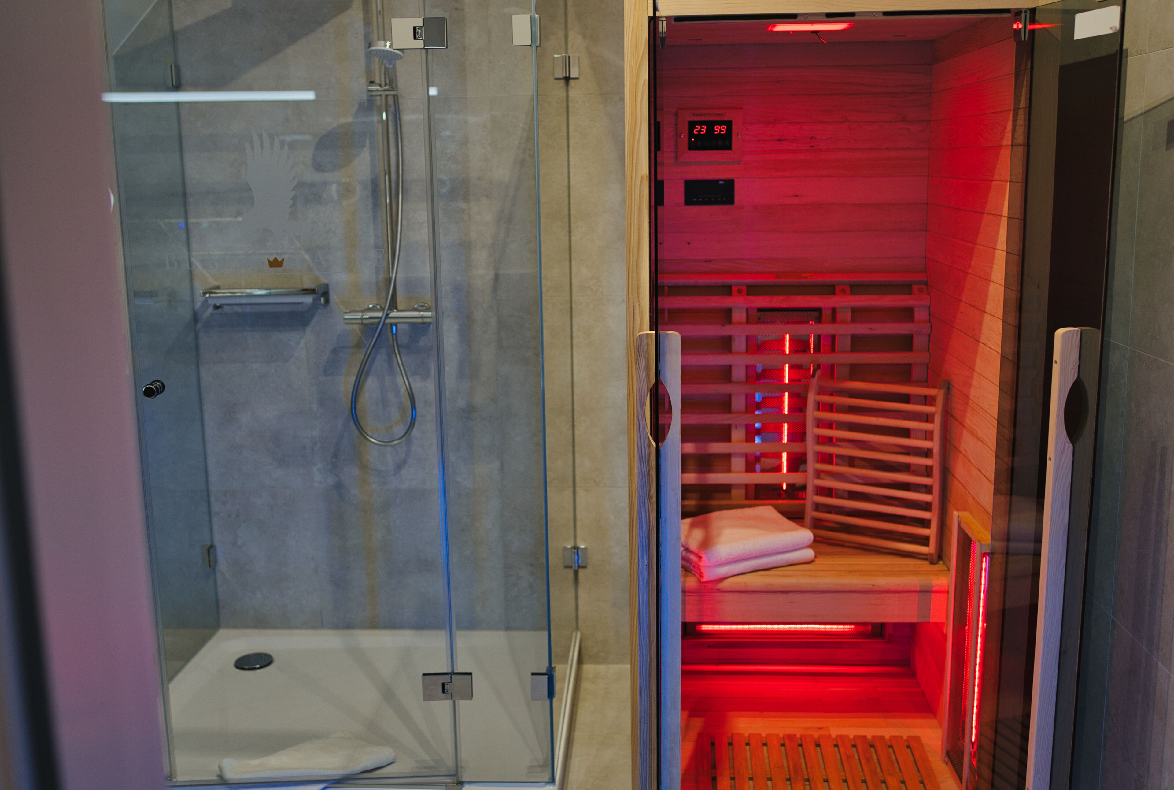 Un sauna doté d’une paroi en verre, d’un banc en bois et d’un écran numérique indiquant la température.
