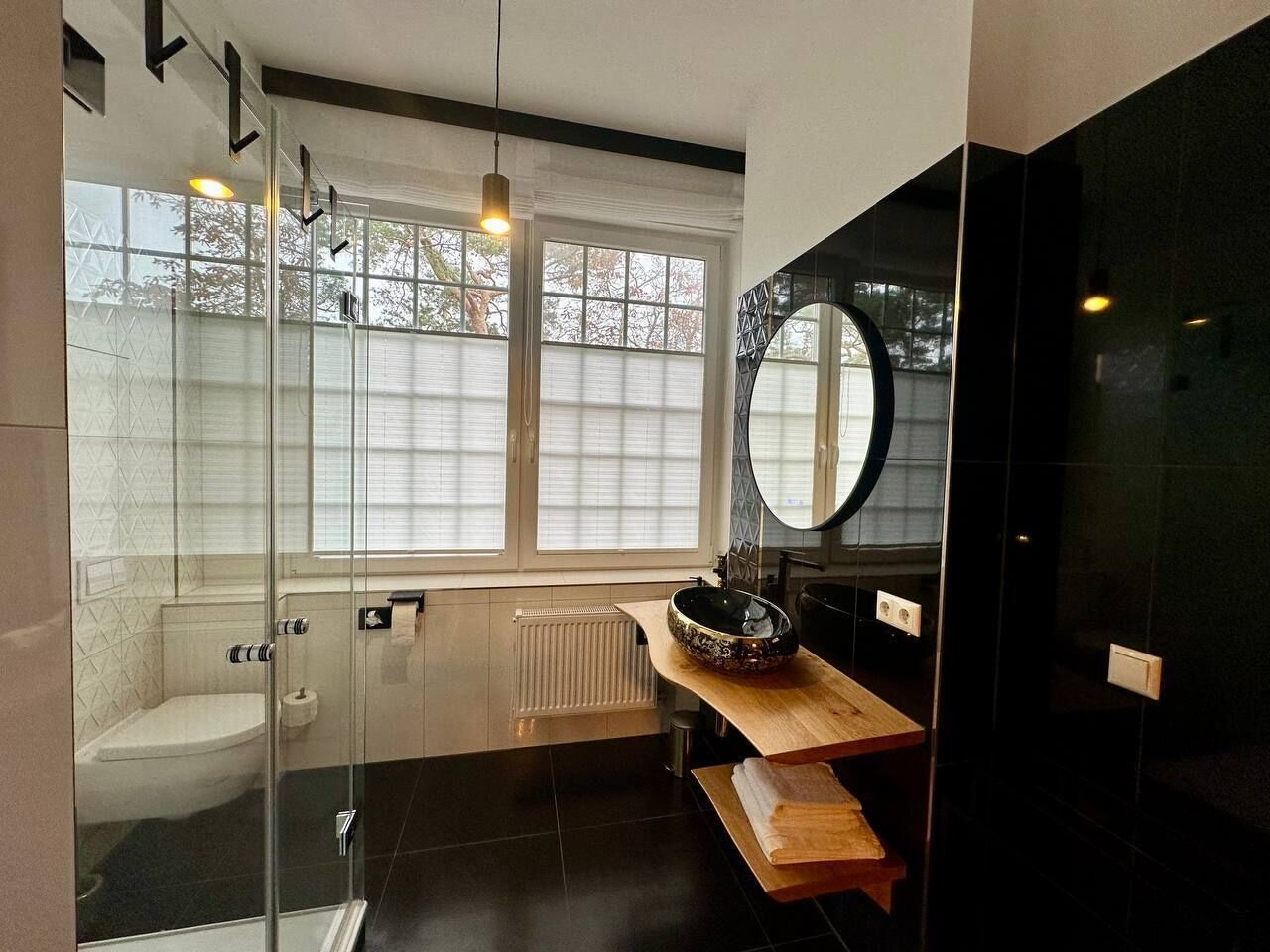 Un baño moderno con cabina de ducha de vidrio, inodoro, lavabo con una pila decorativa y un espejo grande.