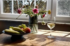 A table with a fruit bowl, a vase with flowers, and a wine glass by a window. - Residence Black Eagle Lubmin (Lubmin)
