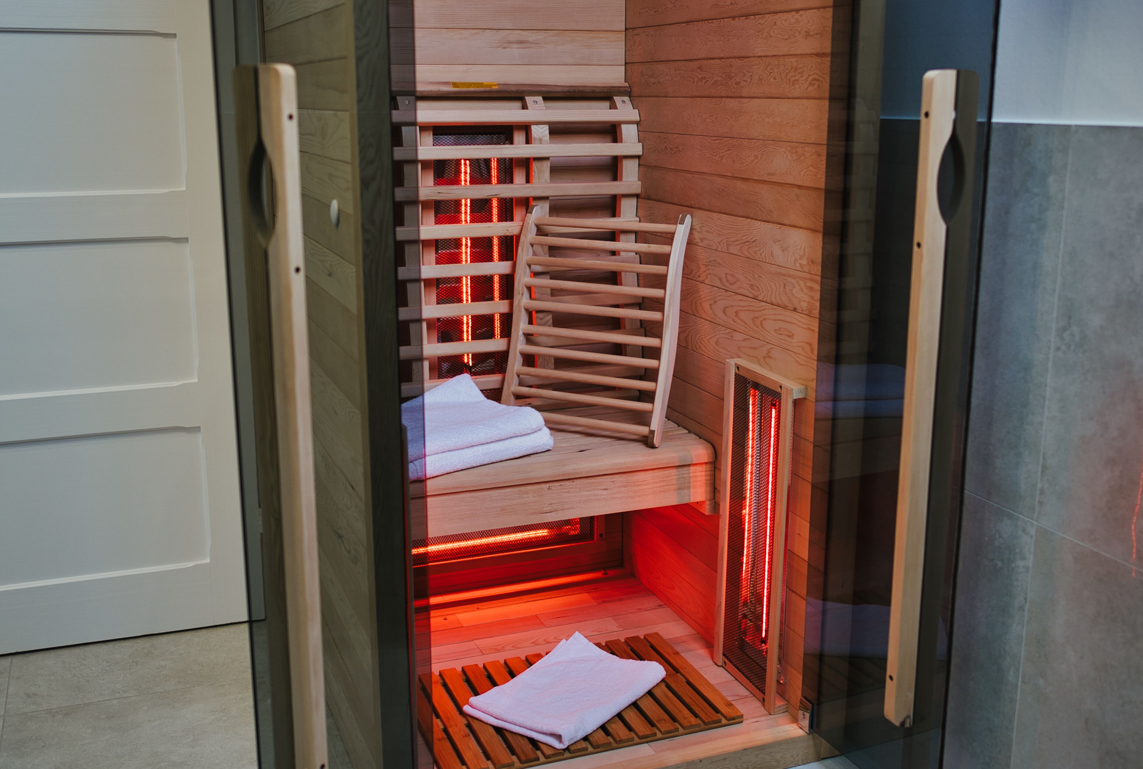 Un sauna avec des bancs en bois et une porte en verre, sur lequel on peut voir une serviette posée sur l’un des bancs.