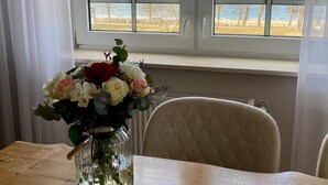 Una habitación con una mesa de madera, un jarrón con flores y vista al mar a través de una ventana.