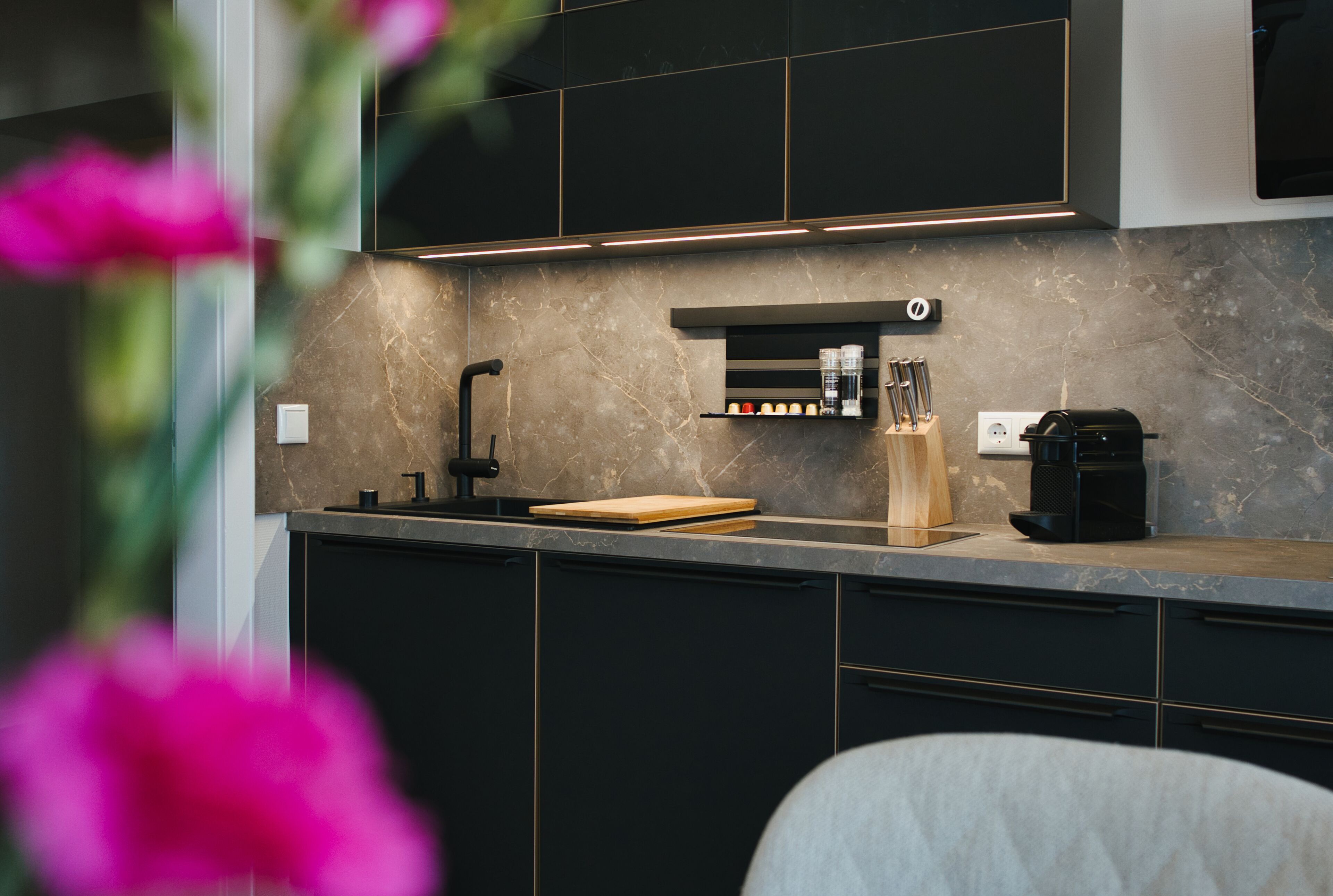 A modern kitchen with dark cabinetry, a marble countertop, a coffee machine, and a knife block.