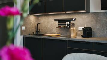 A modern kitchen with dark cabinetry, a marble countertop, a coffee machine, and a knife block.
