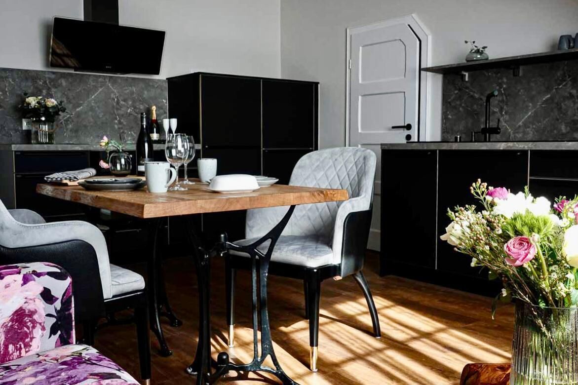 Een moderne keuken met een houten tafel, zwarte kasten en een grijze gestoffeerde stoel.