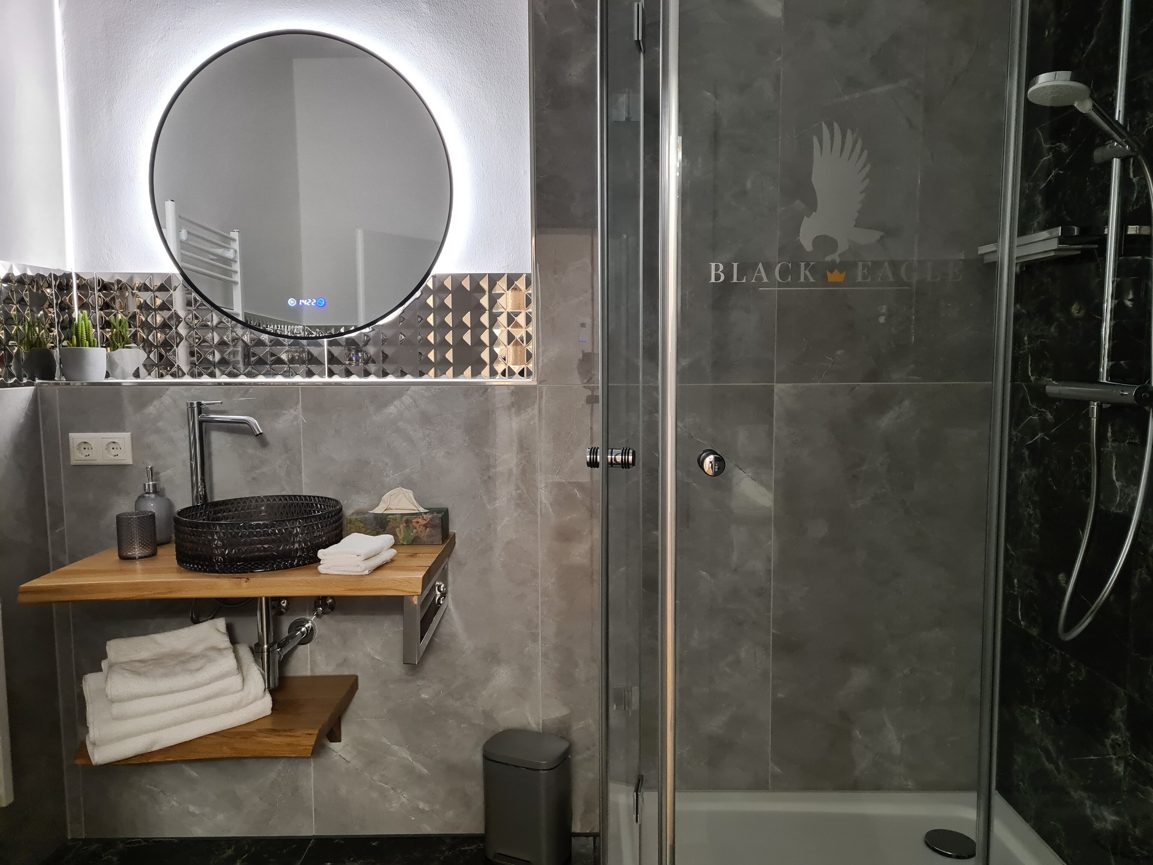 Un baño moderno con un espejo redondo, un lavabo con estante de madera y una zona de ducha con mampara de cristal.