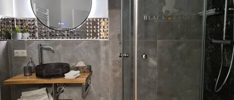 Un baño moderno con un espejo redondo, un lavabo con estante de madera y una zona de ducha con mampara de cristal.