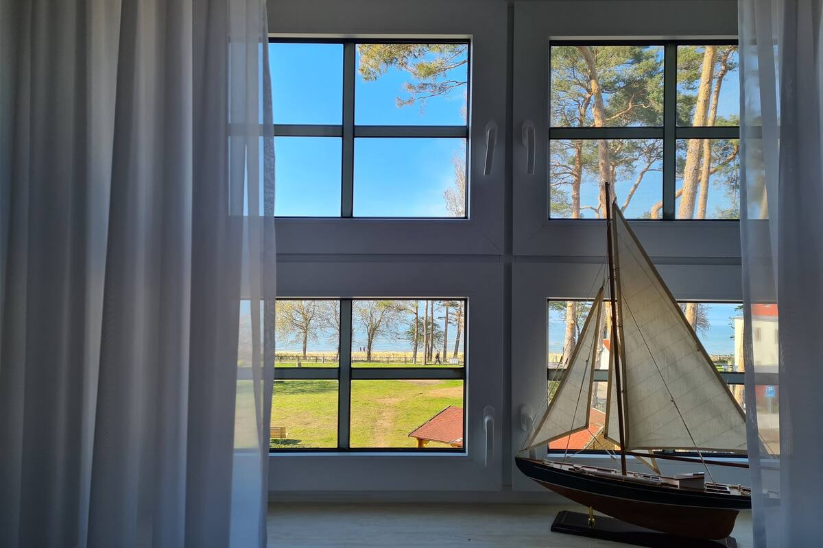 A room with large windows, a sailboat model on a shelf, and a view of a grassy area with trees.