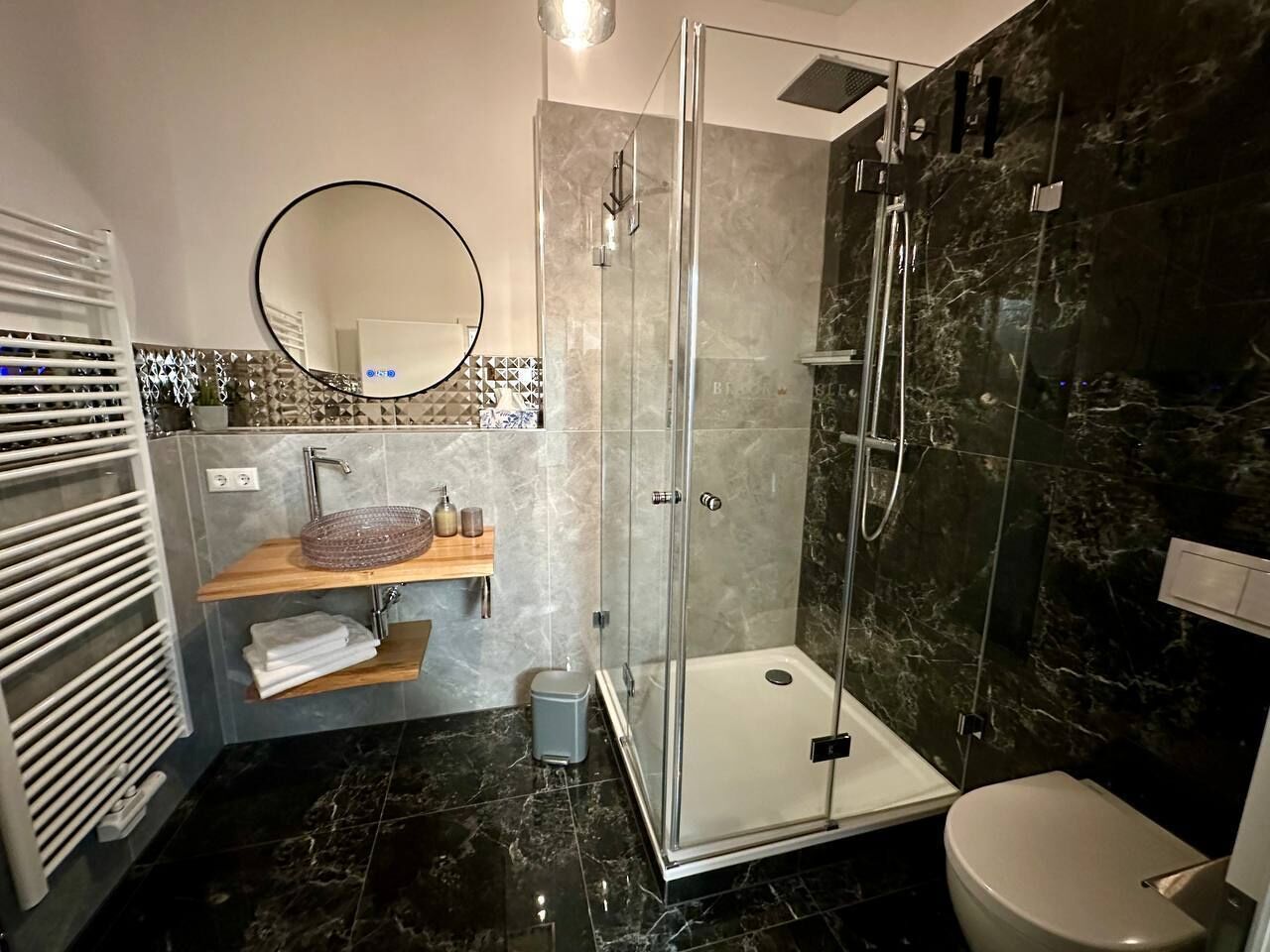 A modern bathroom with a glass-enclosed shower, a white toilet, and a vanity with a mirror and shelves.