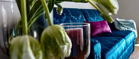 A glass of red liquid on a table with a blue sofa and a plant in the background.