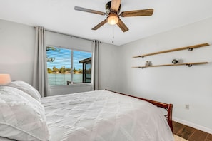 Une chambre à coucher avec un lit, un ventilateur de plafond, une fenêtre avec des rideaux et une vue sur une maison.