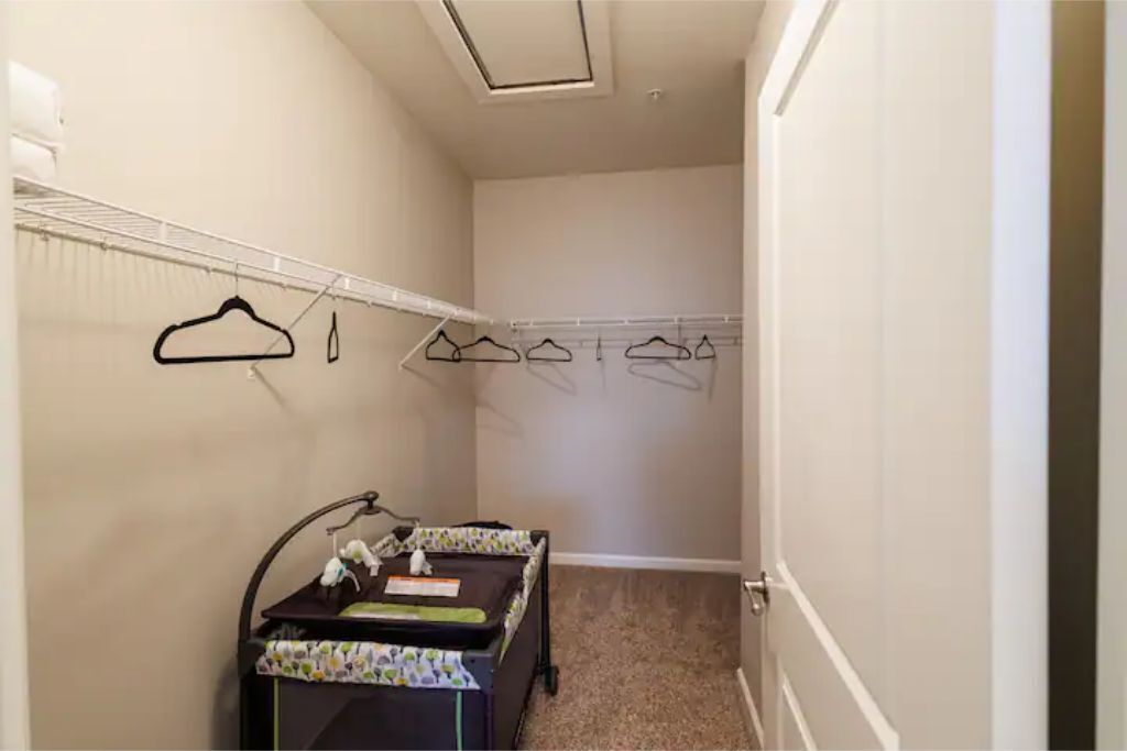 A small, narrow room with a walk-in closet, a desk with a chair, and a radiator.