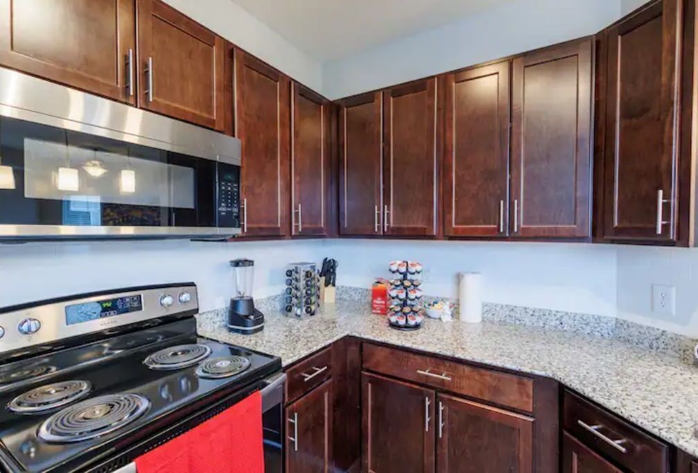 A kitchen with dark wood cabinets, a stainless steel microwave, a black stove, and granite countertops.