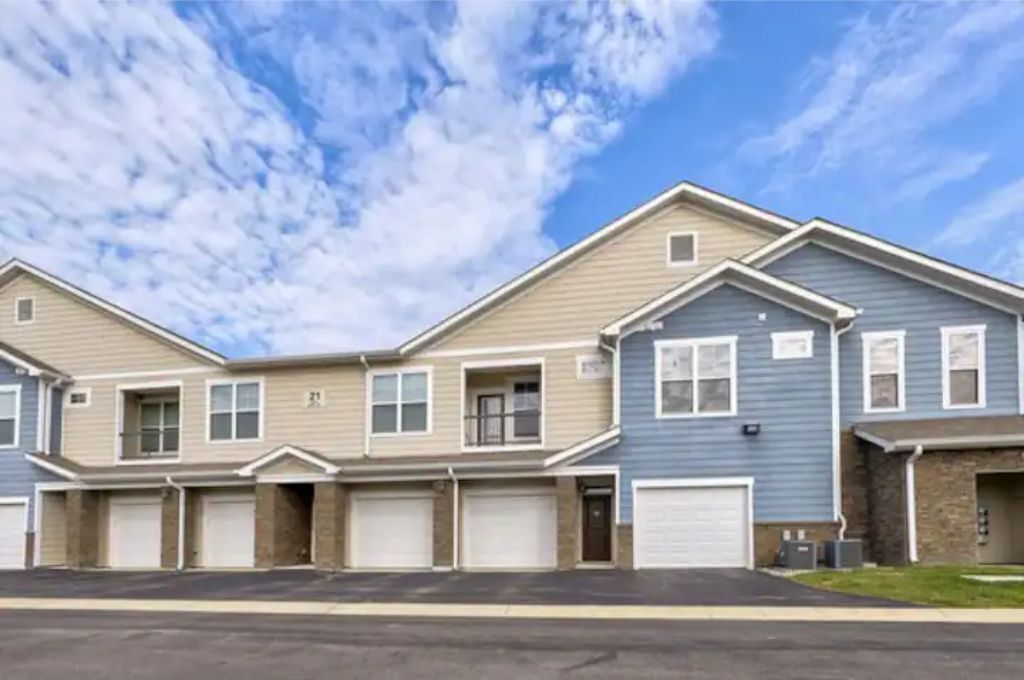 A row of townhouses with attached garages, a clear sky, and a well-maintained lawn.