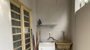 A small, enclosed bathroom with a toilet, sink, and shower area. There are cleaning tools and a shelf above the sink. - AconchegoF (Goiânia)
