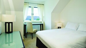 A hotel room with a bed, desk, chair, and a window with curtains. - Ring of Kerry Holiday Cottages (Greenane)