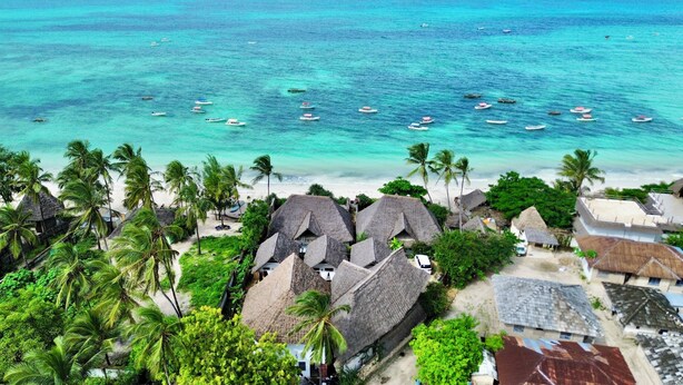Ein tropischer Strand mit strohgedeckten Hütten und einem klaren türkisblauen Meer.