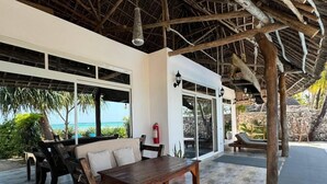An outdoor covered area with a wooden table and chairs, a fire extinguisher, and a view of the ocean. - Bitcoin Beach Hotel Zanzibar (Michamvi)