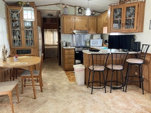 Compact kitchen with wooden cabinetry, central island, and seating area, featuring a microwave, stove, and sink.
