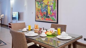 Zona pranzo con sedie in vimini, un tavolo in vetro e prodotti per la colazione, tra cui pane, frutta e succo di frutta.