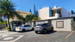 Un’area di parcheggio con due auto parcheggiate di fronte a un edificio dal design moderno, caratterizzato da un muro in pietra e un emblema decorativo.