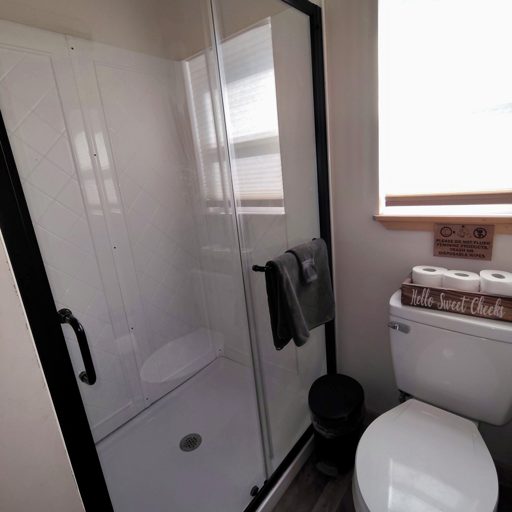 Kylpyhuoneessa on lasiseinällä varustettu suihku, wc ja kyltti, jossa kehotetaan olemaan heittämättä naisten hygieniatuotteita wc:hen.